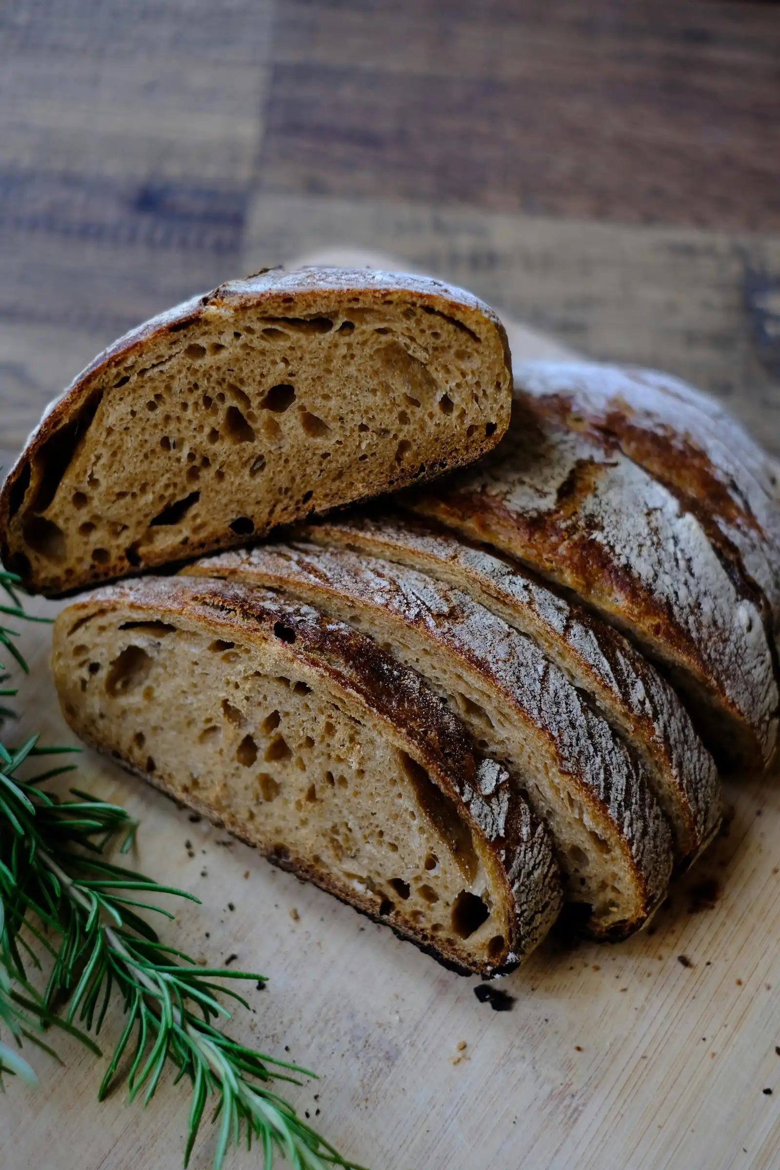 Freshly baked artisan sourdough bread with beautiful open crumb, sliced and displayed with rosemary